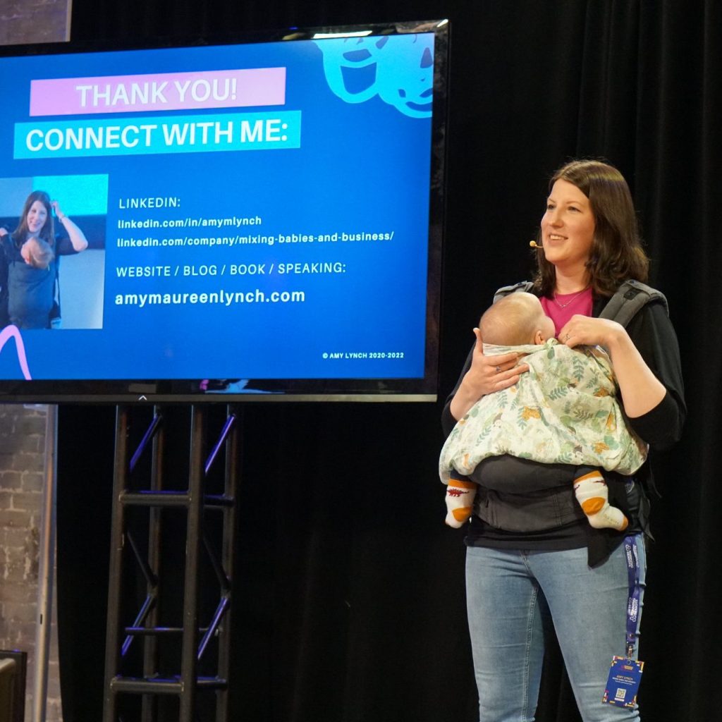 Amy Lynch presenting a 'Remote Work With Kids' keynote at the Running Remote Conference in 2022, while babywearing her third child at four months old.